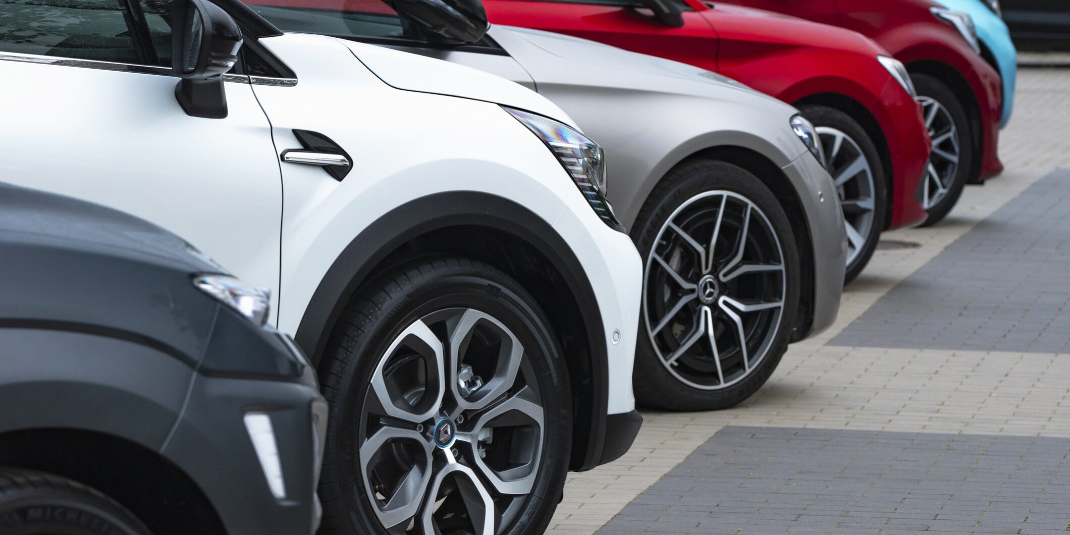 Row of modern parked cars in various colours, viewed from the front side