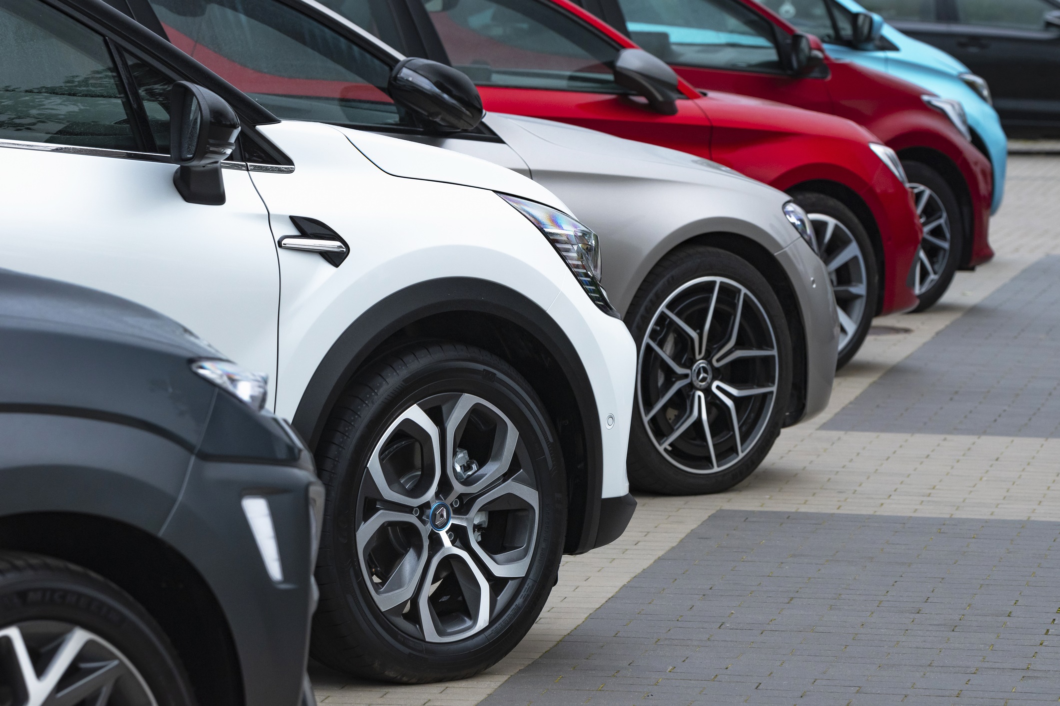 Row of modern parked cars in various colours, viewed from the front side
