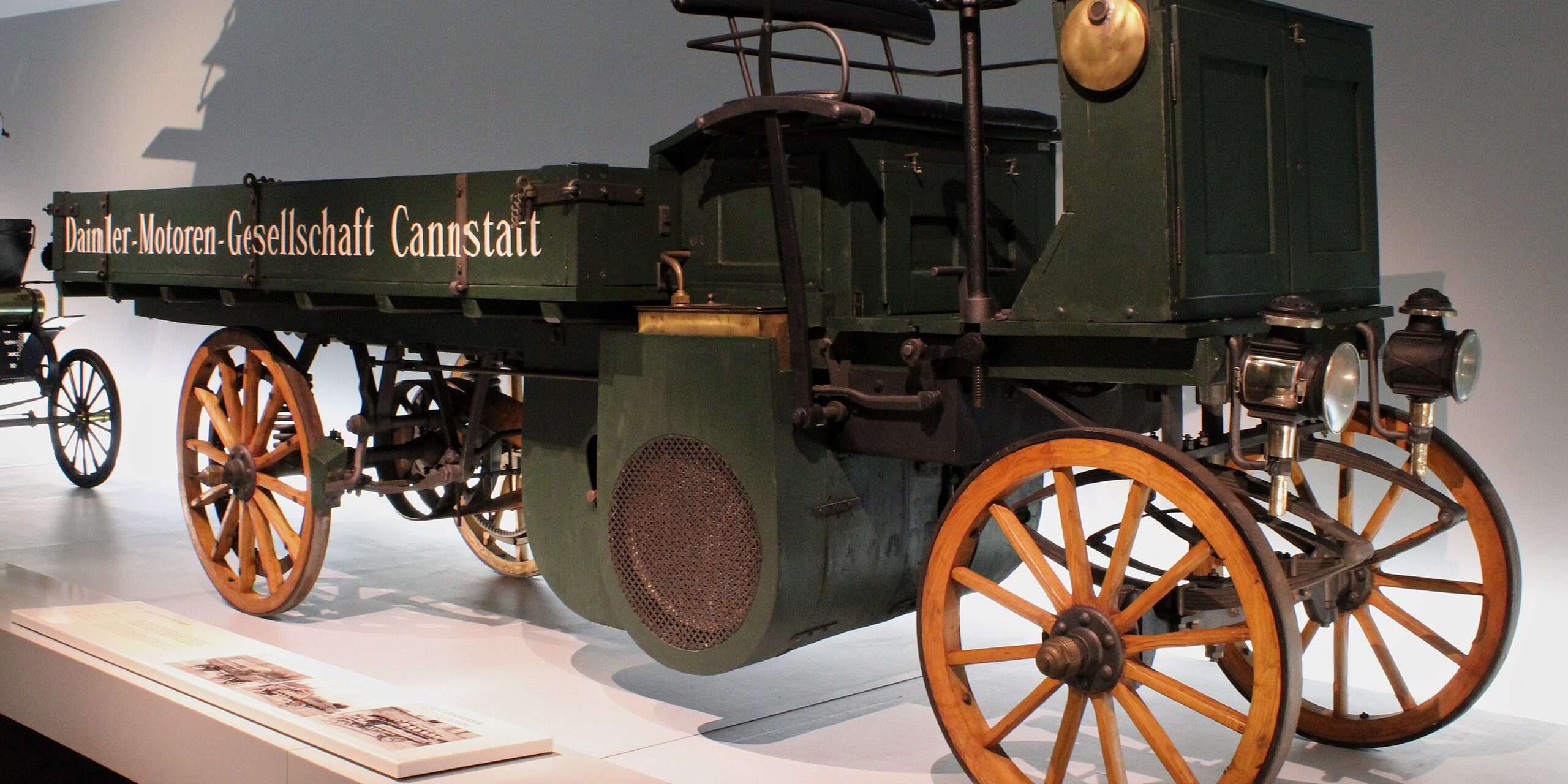 A vintage Daimler truck with wooden wheels and a green body, displayed prominently in a museum.
