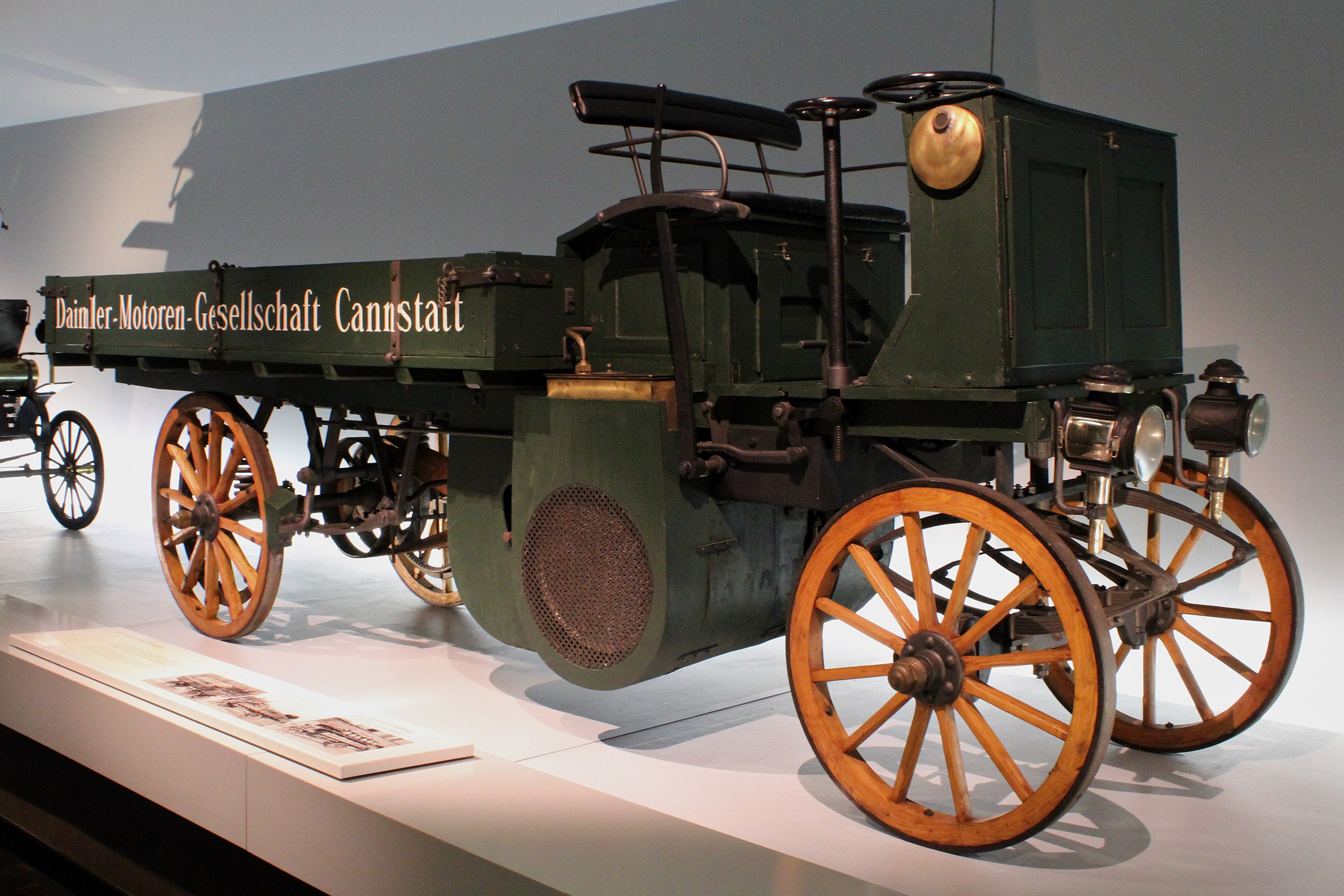 A vintage Daimler truck with wooden wheels and a green body, displayed prominently in a museum.