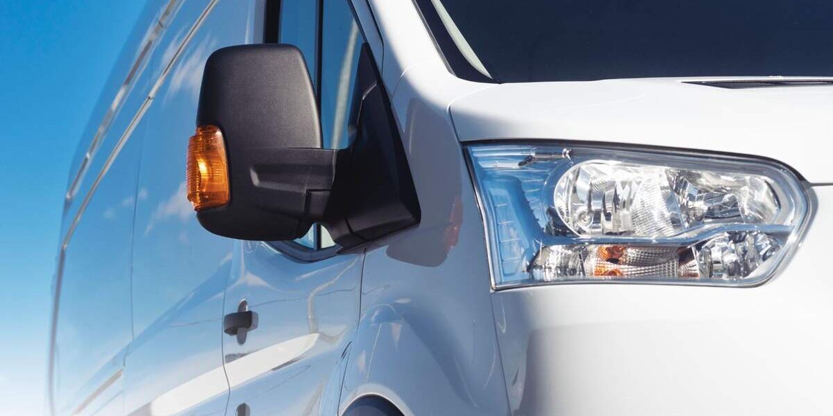 Close-up of a van's wing mirror and headlight with a clear blue sky in the background