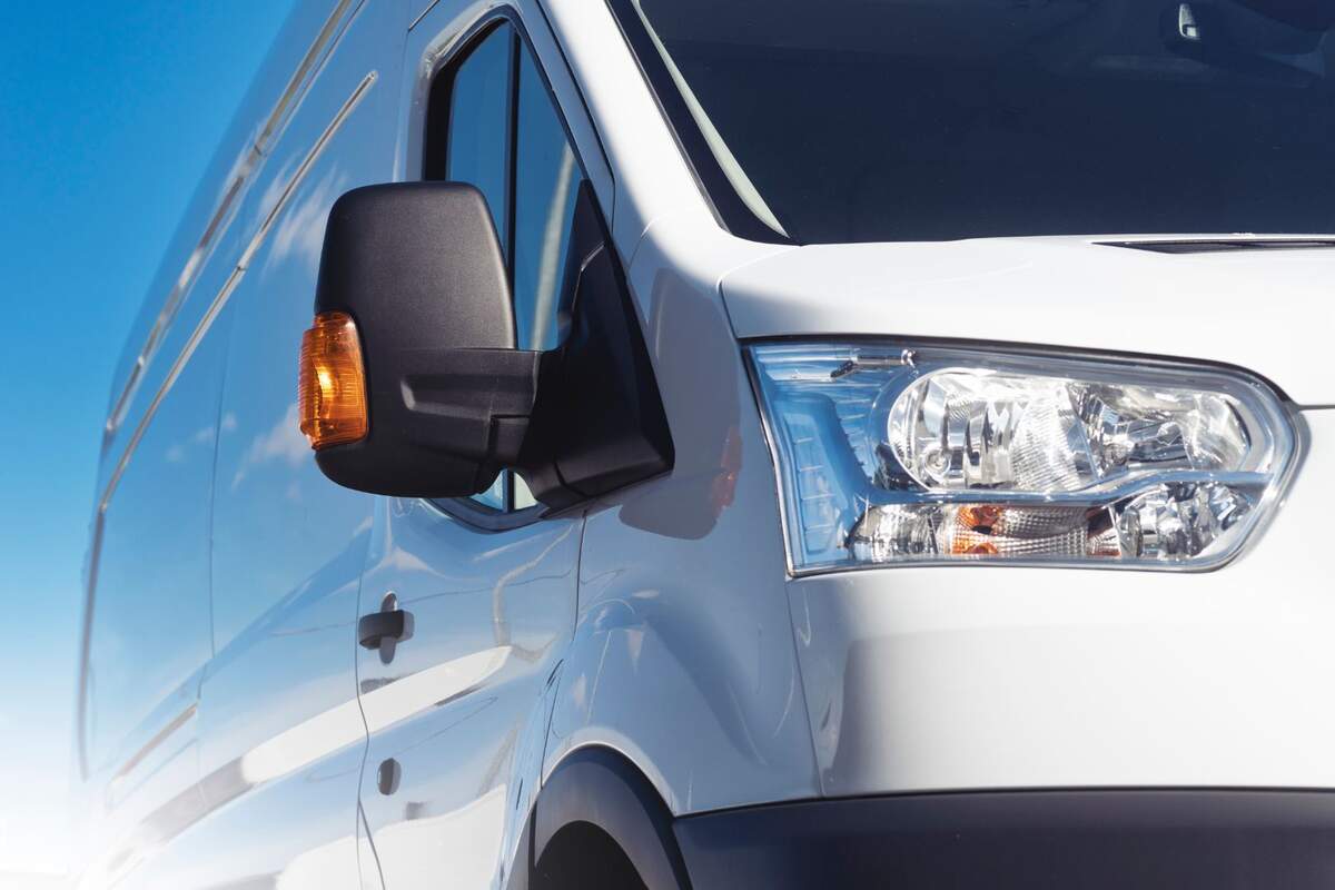 Close-up of a van's wing mirror and headlight with a clear blue sky in the background