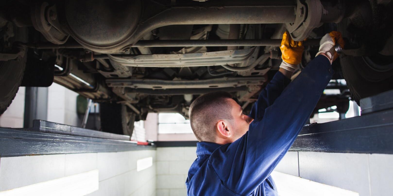Man wearing gloves fixing a car part while working in an inspection pit