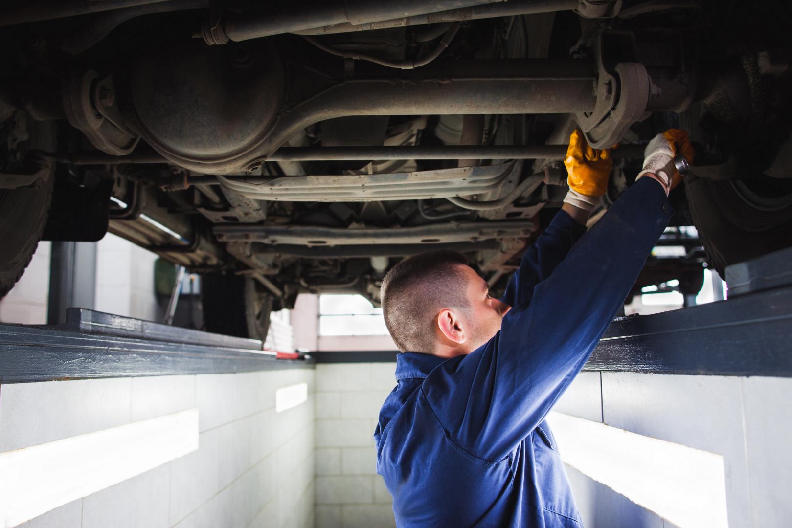 Man wearing gloves fixing a car part while working in an inspection pit