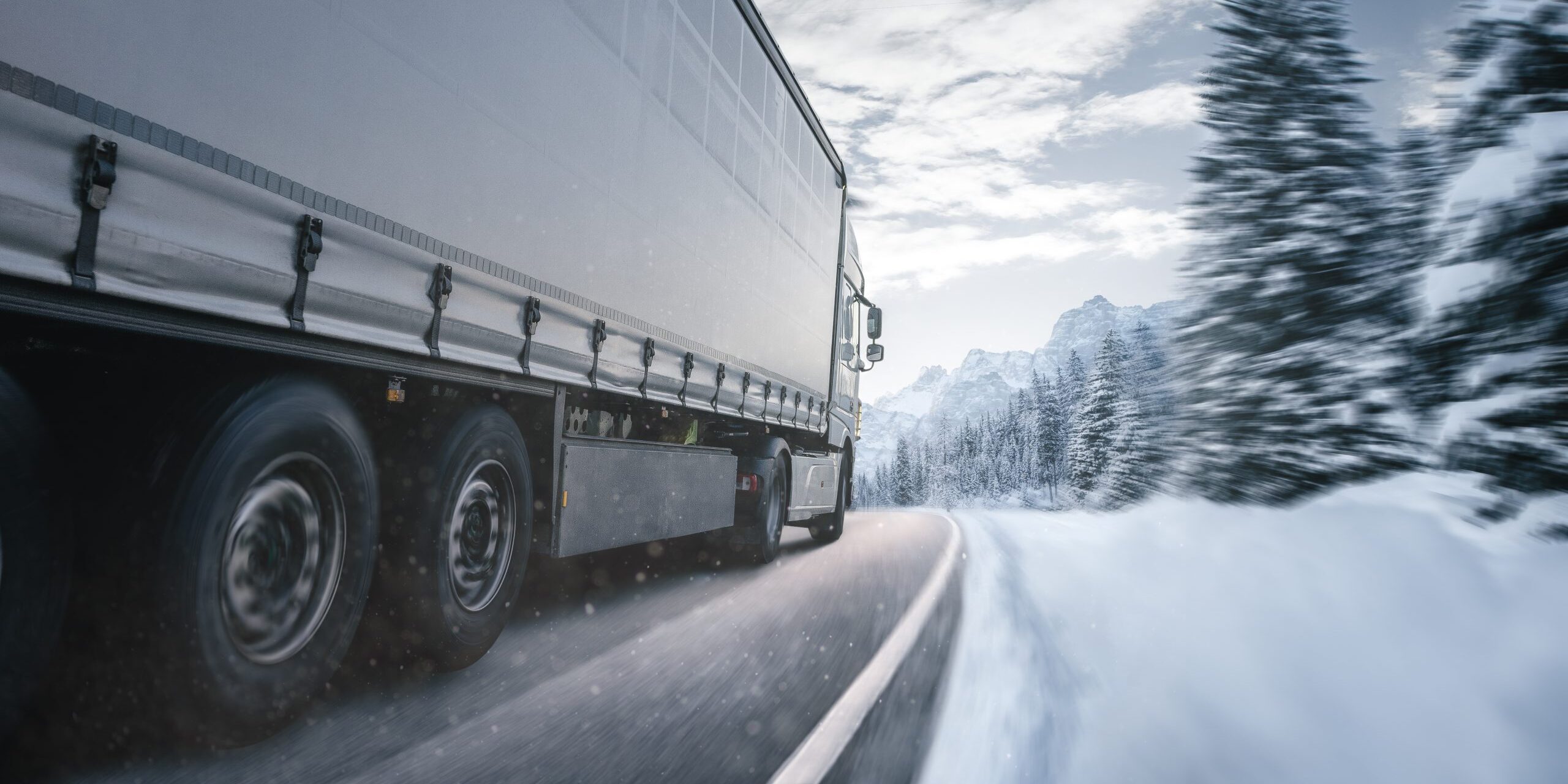 Articulated lorry driving through a snowy mountain road in winter conditions.