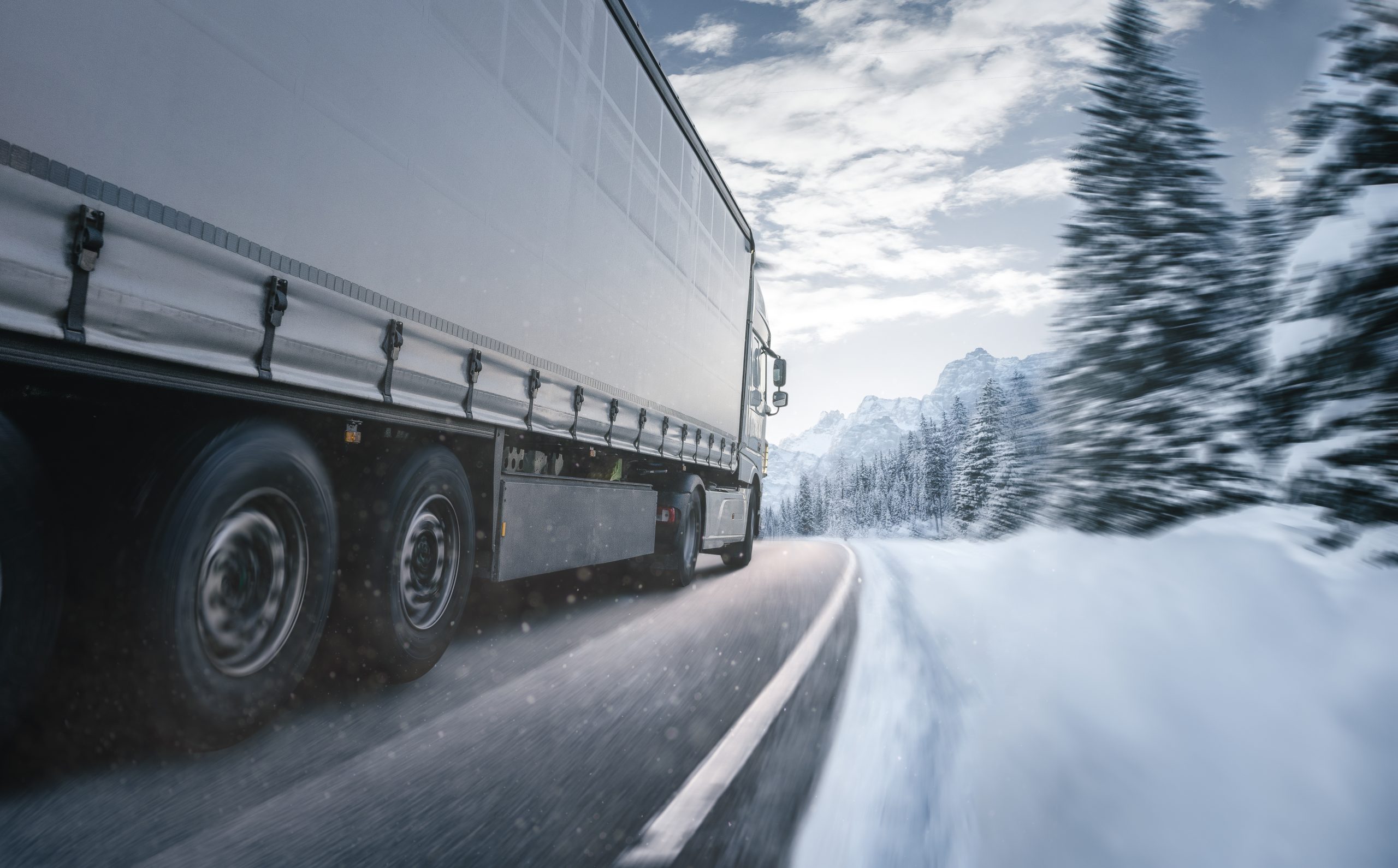 Articulated lorry driving through a snowy mountain road in winter conditions.