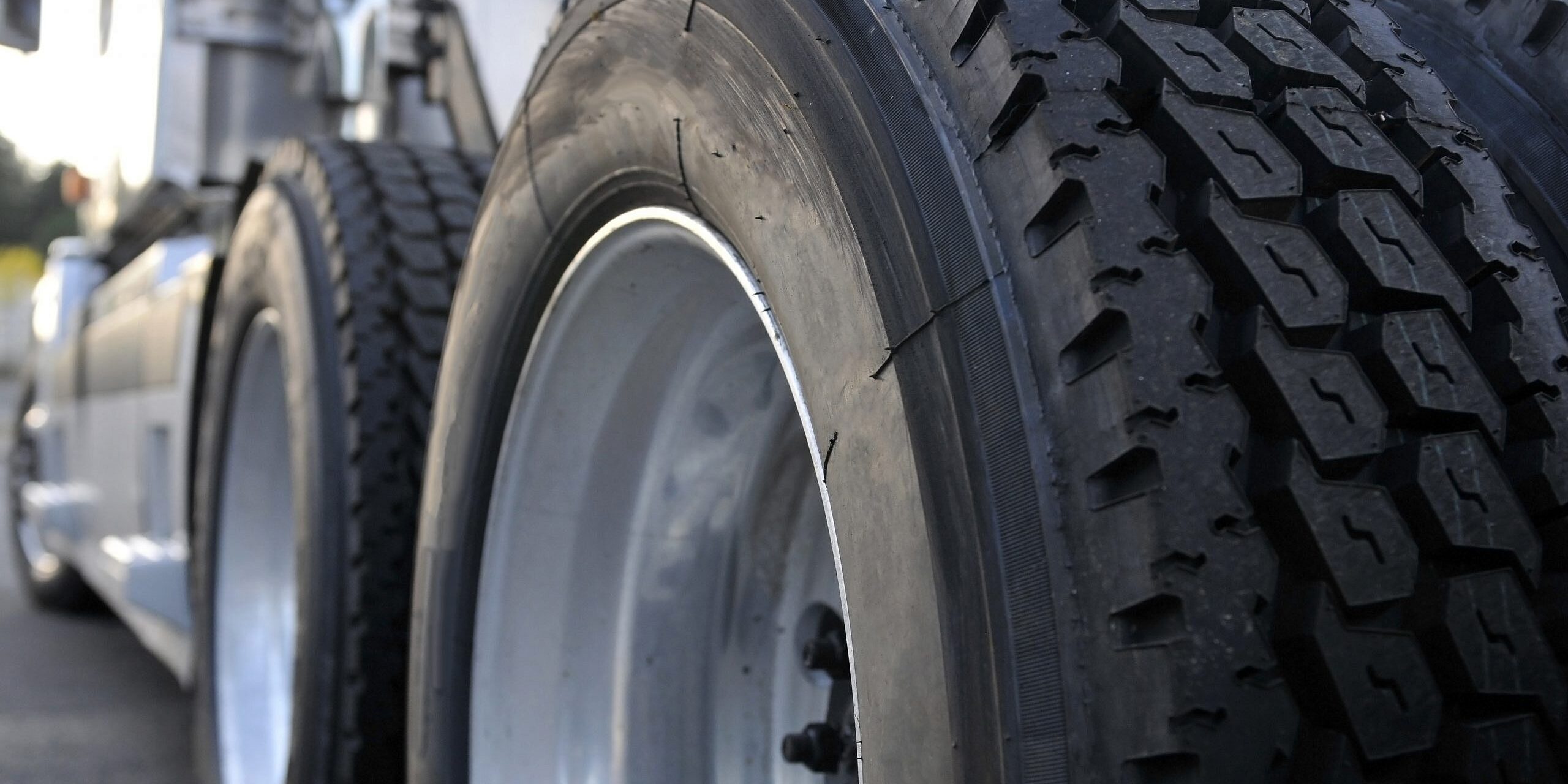 Close-up of heavy-duty lorry tyres with deep tread patterns on a paved road.