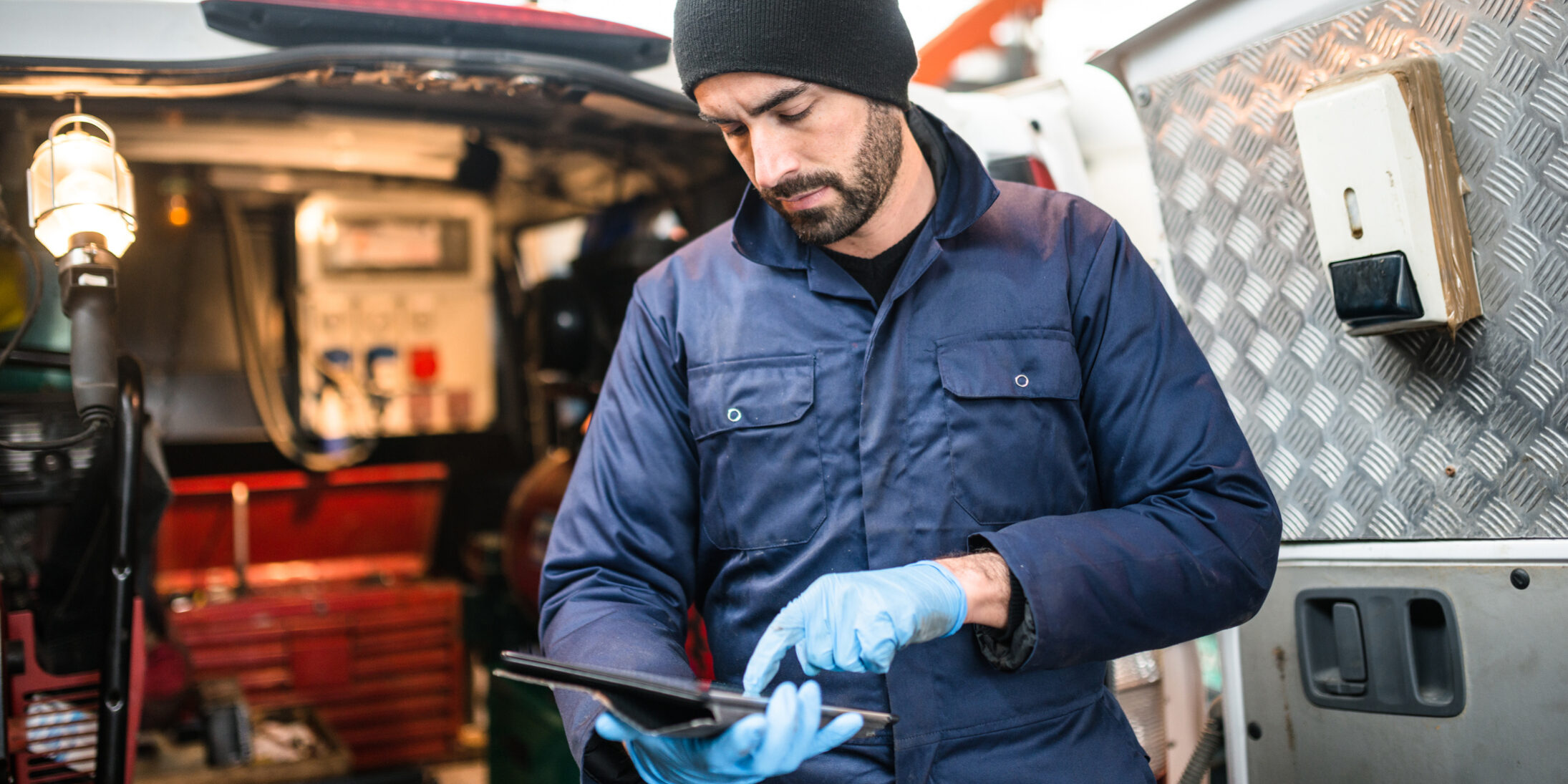 Man wearing blue plastic gloves using an iPad with a van in the background
