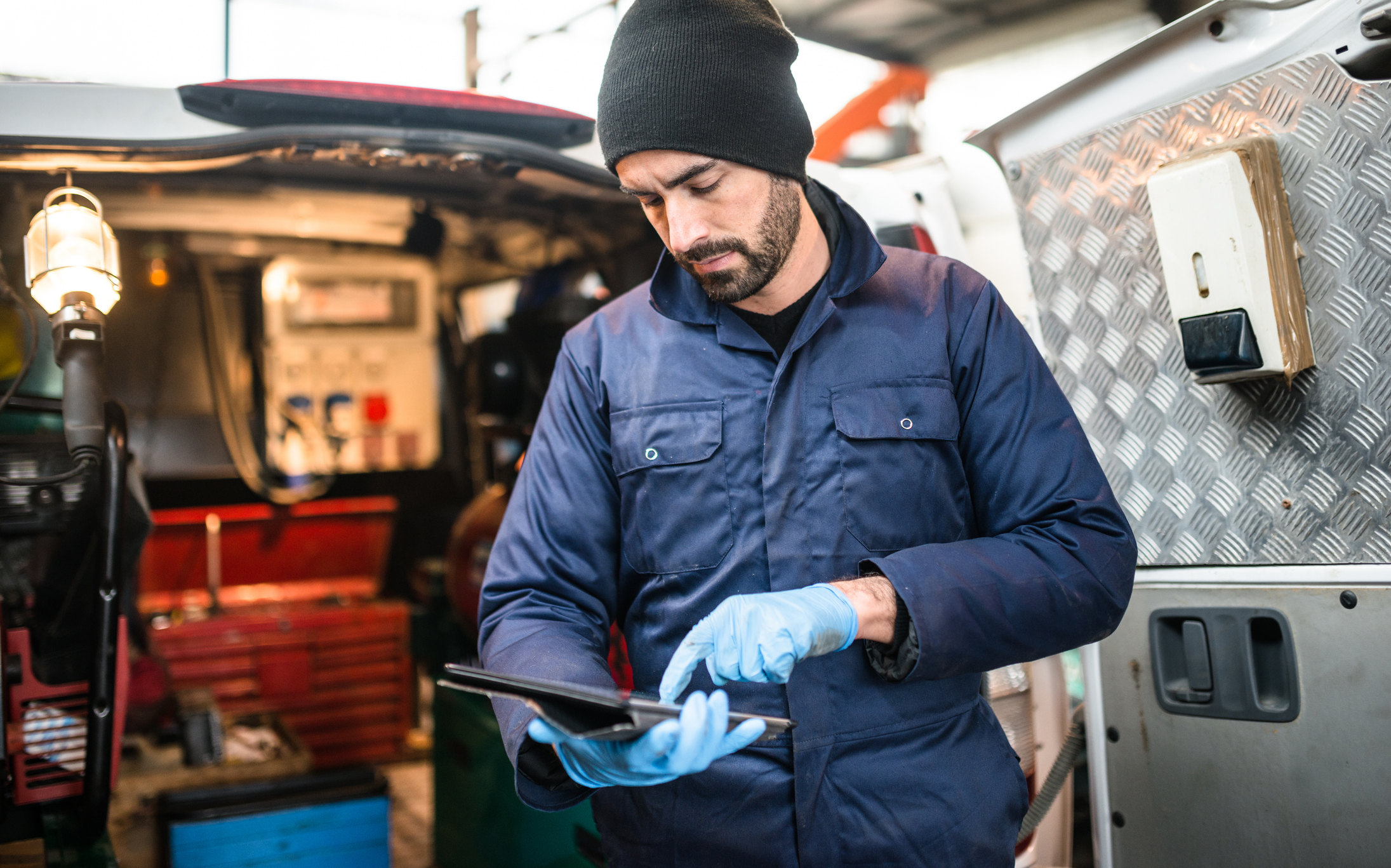 Man wearing blue plastic gloves using an iPad with a van in the background