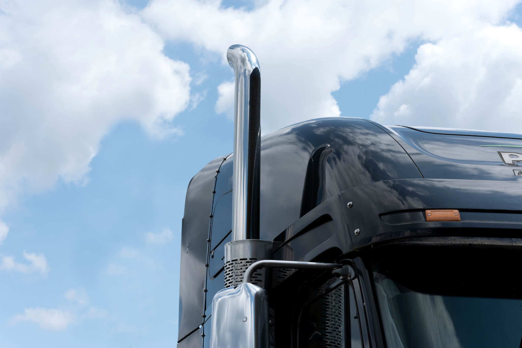 Close-up of a black lorry cab with chrome exhaust pipe against a blue sky.