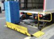 Delivery truck with open tail lift unloading stacked blue crates onto a high street.