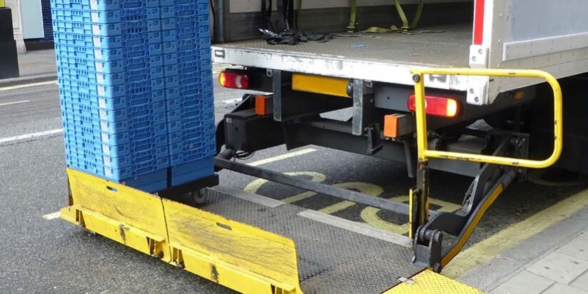 Delivery truck with open tail lift unloading stacked blue crates onto a high street.